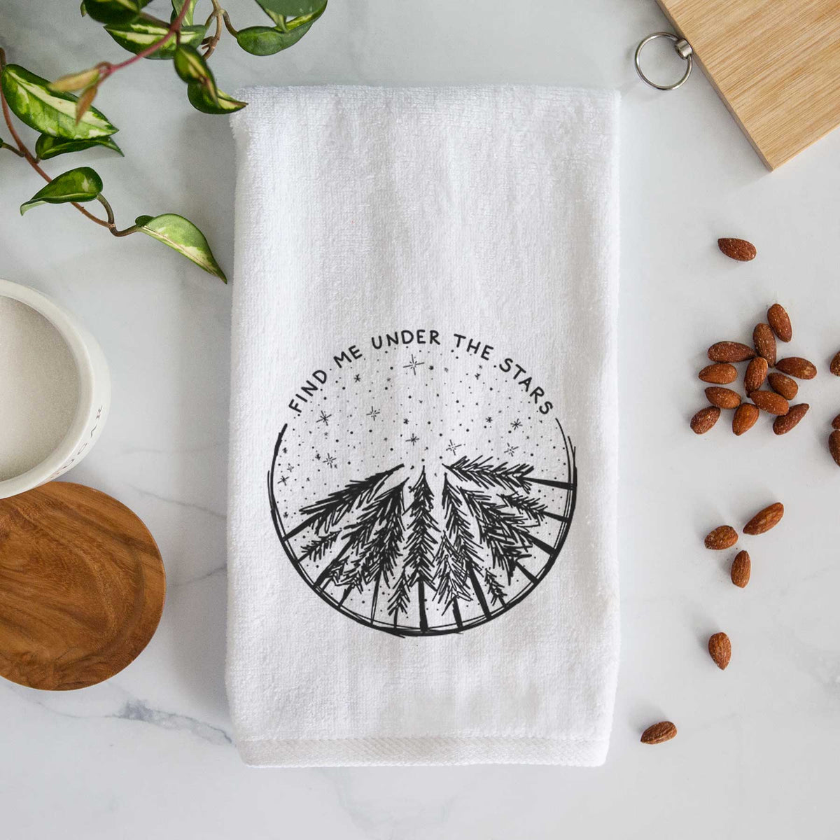 White hand towel printed with a circle of pine trees under a starry sky, with the words Find Me Under the Stars.