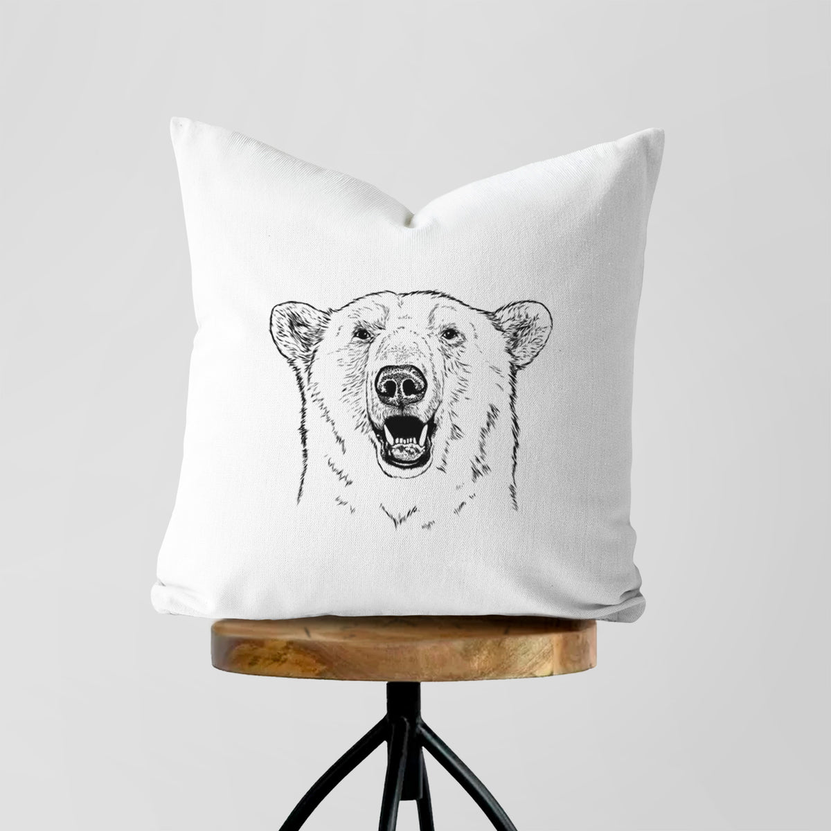 White pillow cover printed with a black ink portrait of a smiling polar bear's face, on a wooden stool.