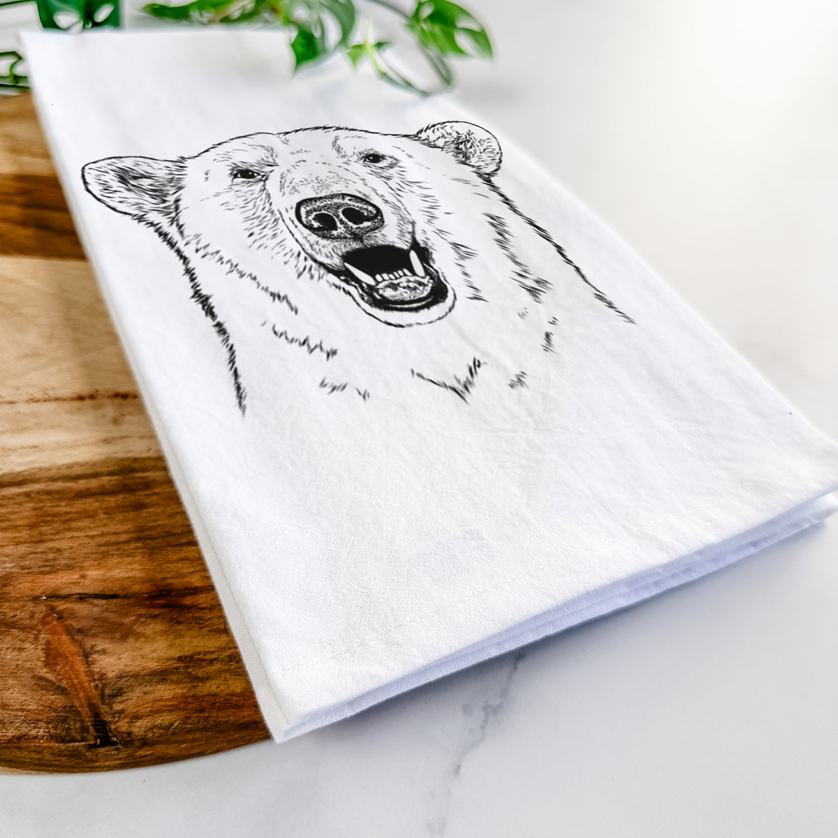 Close-up of a folded white tea towel on a wooden board, showing a black ink portrait of a smiling polar bear's face.