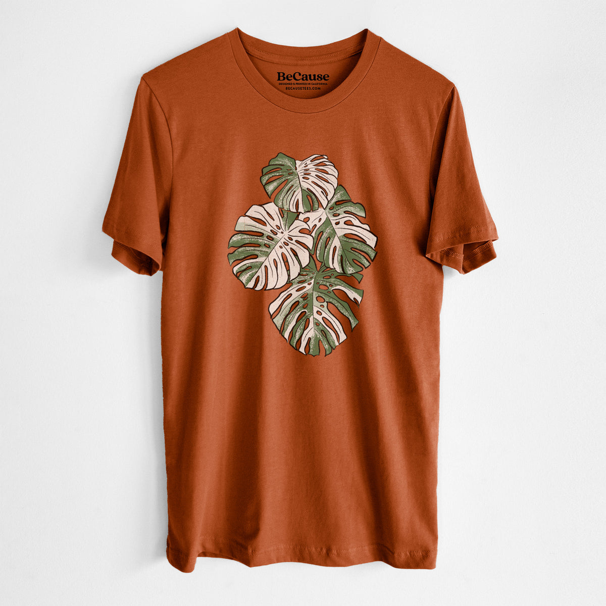 Autumn lightweight cotton t-shirt laid flat, printed with a full-color illustration of a variegated Monstera leaf in green and white.