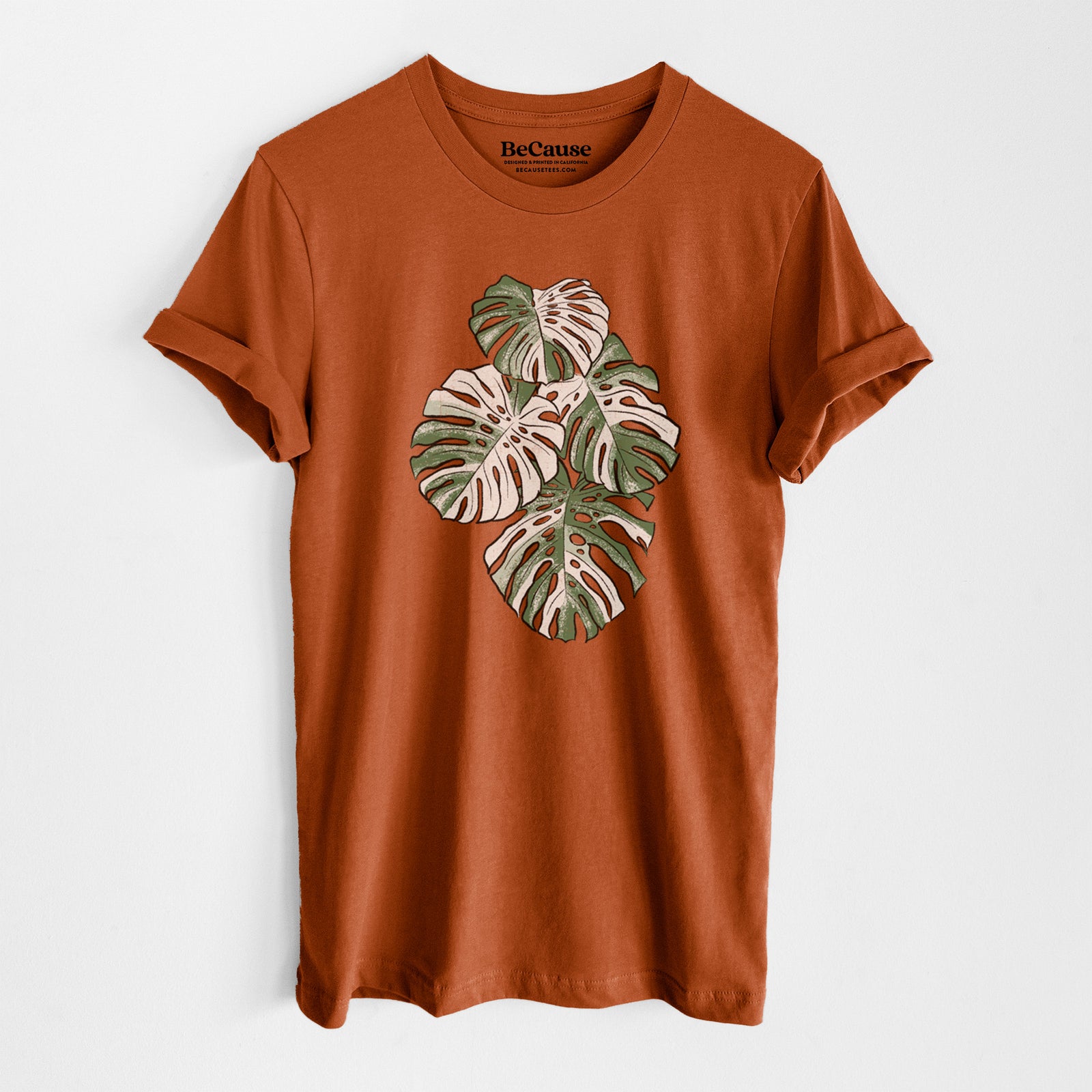 Autumn lightweight cotton t-shirt laid flat, printed with a full-color illustration of a variegated Monstera leaf in green and white.