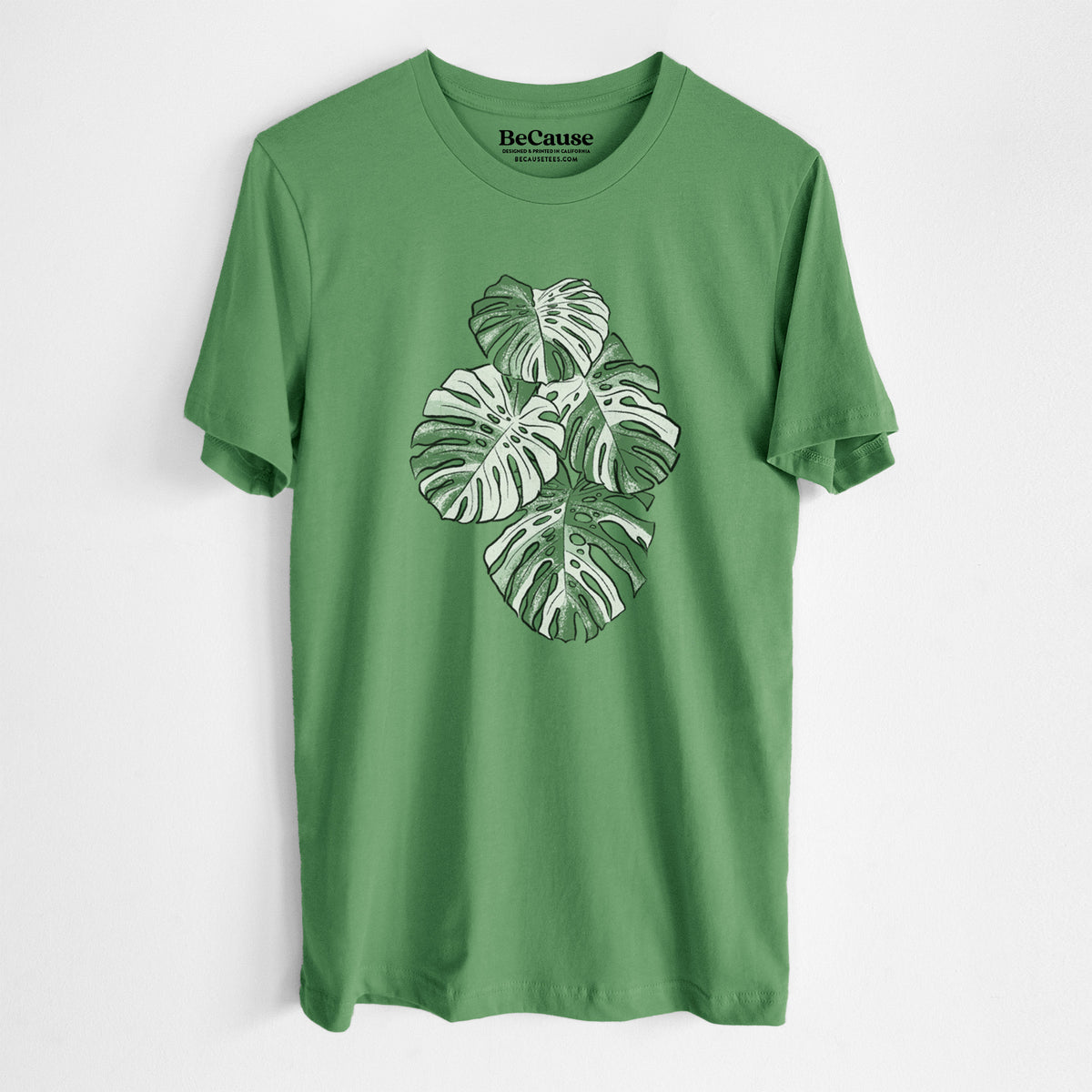 Leaf green lightweight cotton t-shirt laid flat, printed with a full-color illustration of a variegated Monstera leaf in green and white.
