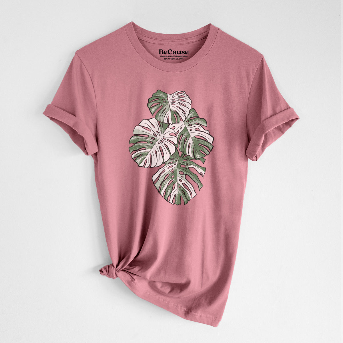 Mauve pink lightweight cotton t-shirt laid flat with the sleeves rolled, printed with a full-color illustration of a variegated Monstera leaf in green and white.