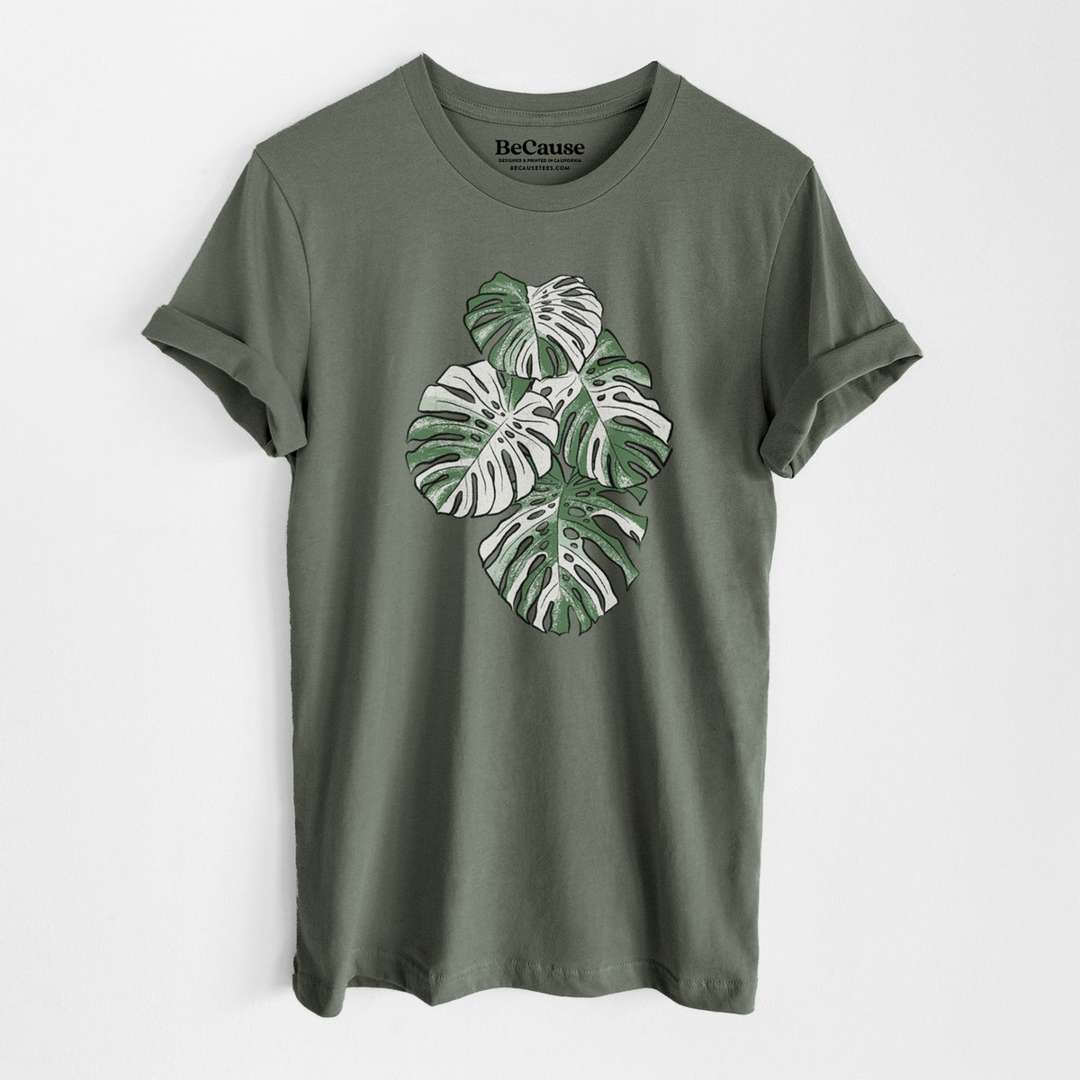 Military green lightweight cotton t-shirt laid flat, printed with a full-color illustration of a variegated Monstera leaf in green and white.