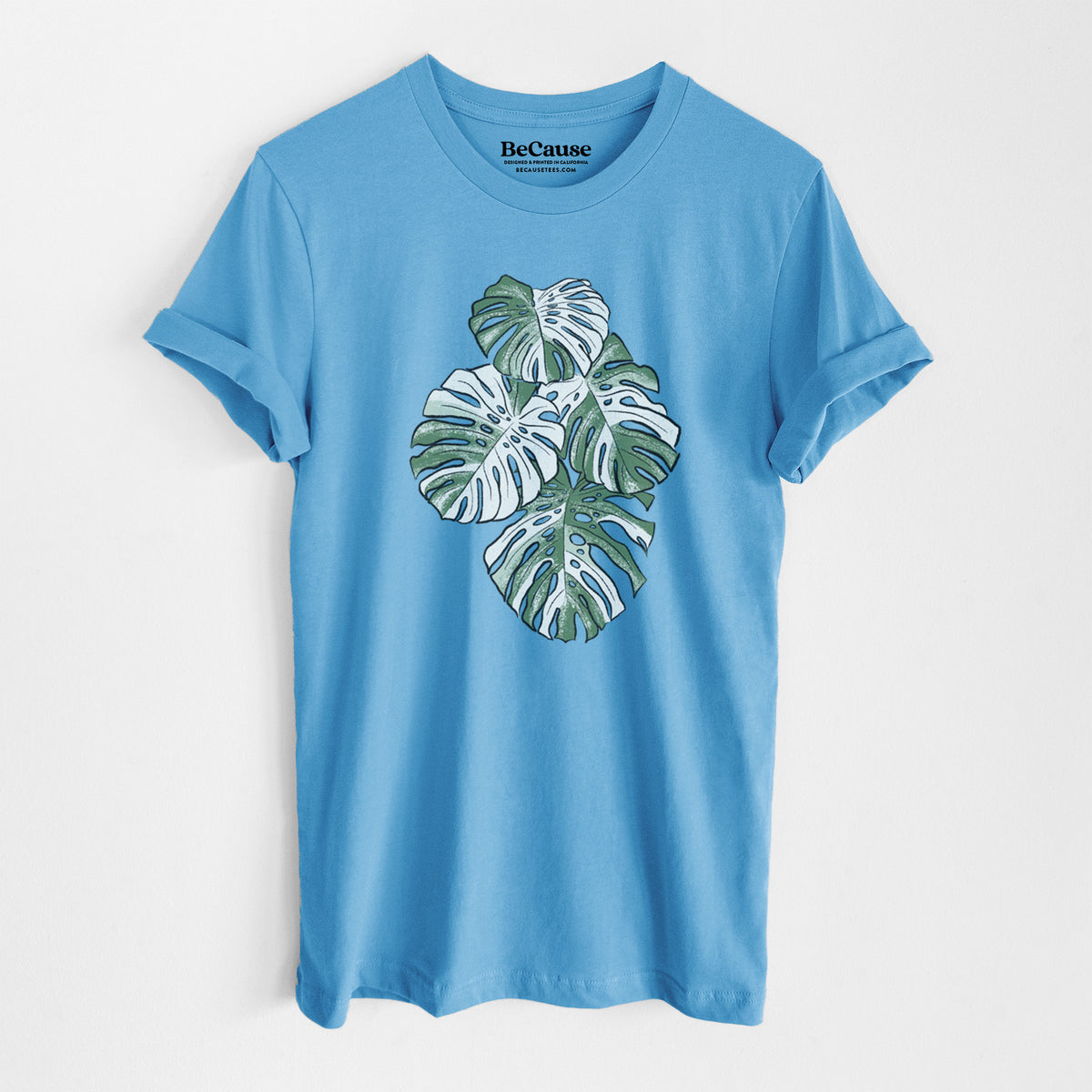 Ocean blue lightweight cotton t-shirt laid flat, printed with a full-color illustration of a variegated Monstera leaf in green and white.