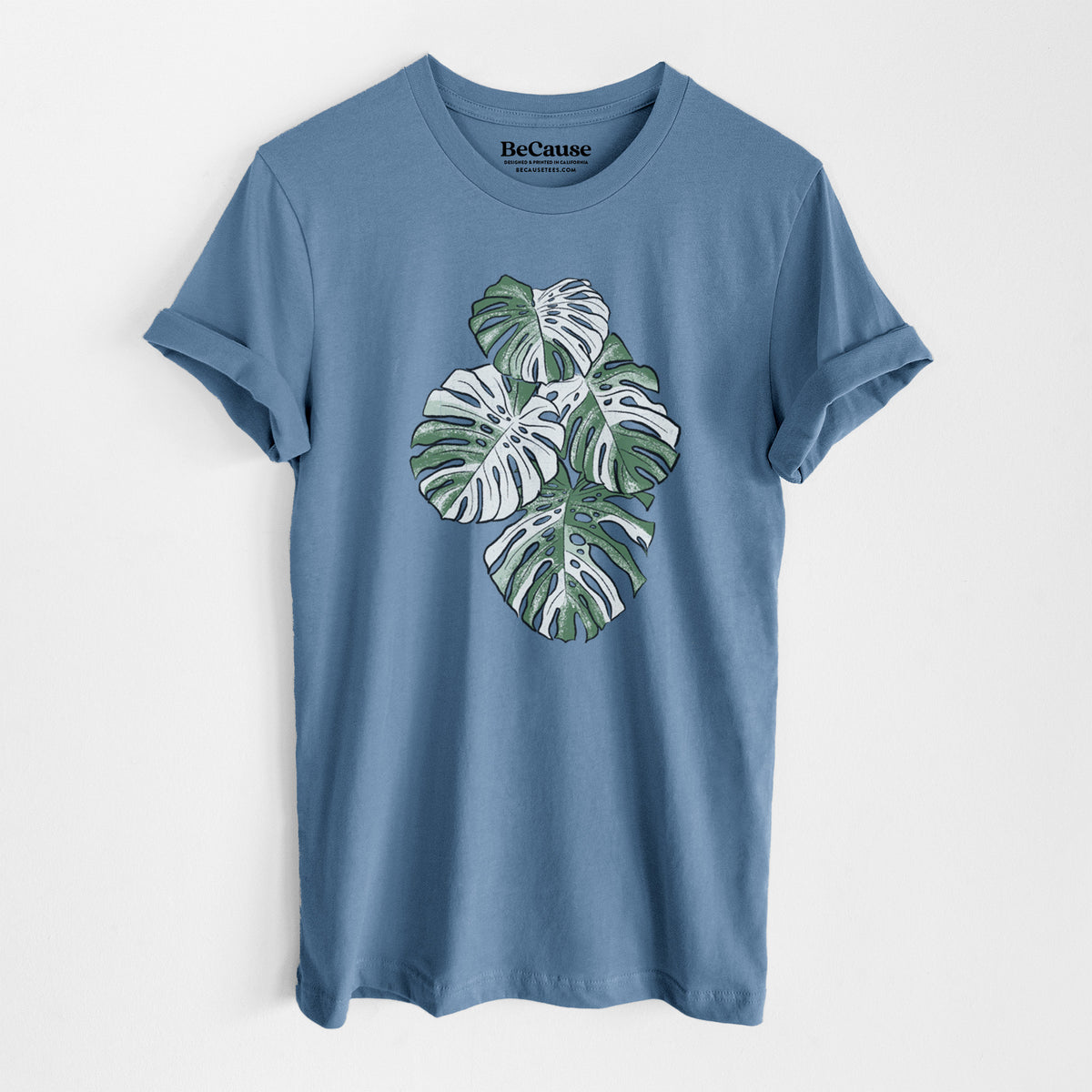 Steel blue lightweight cotton t-shirt laid flat, printed with a full-color illustration of a variegated Monstera leaf in green and white.