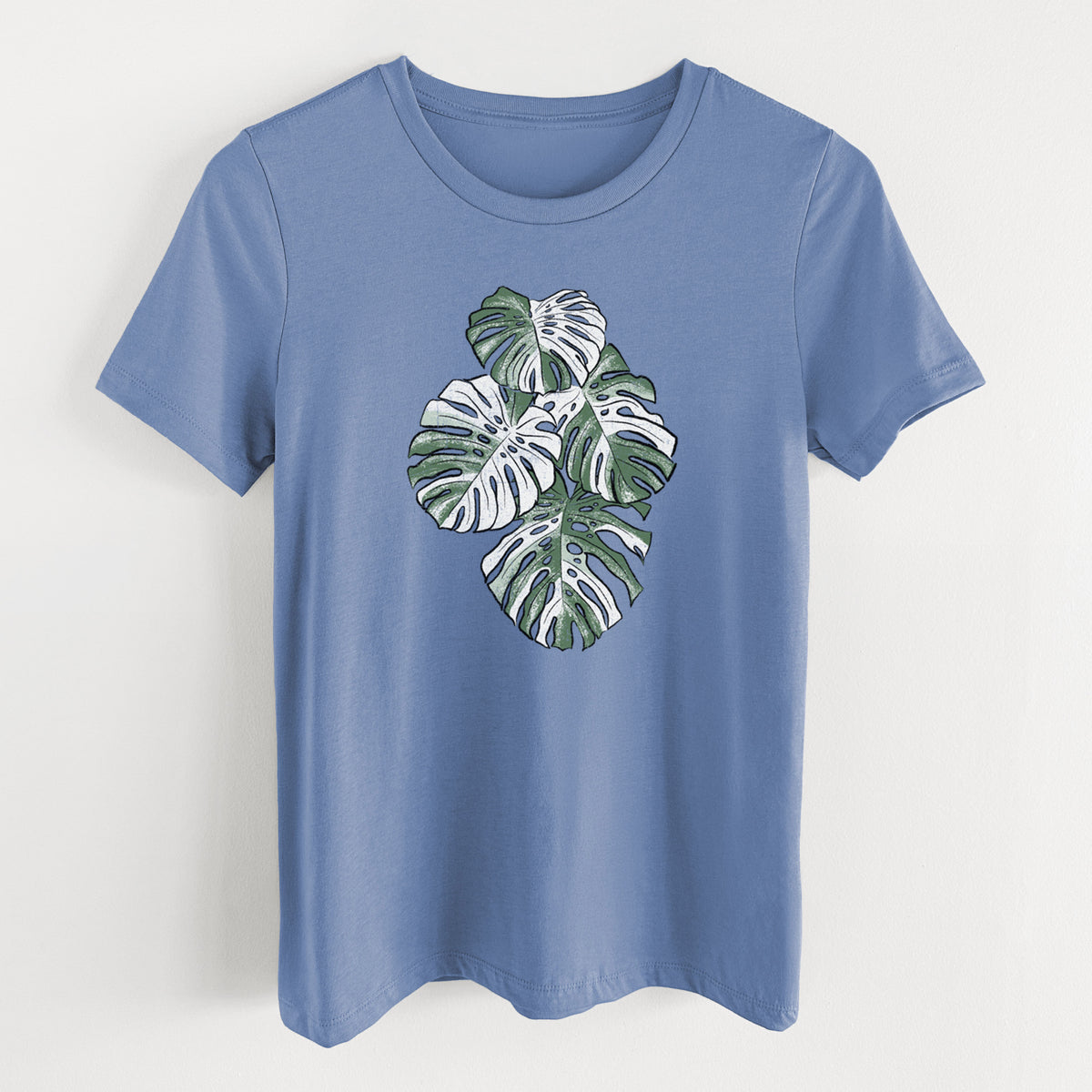 Blue bell women's relaxed fit cotton t-shirt laid flat, printed with a full-color illustration of a variegated Monstera leaf in green and white.