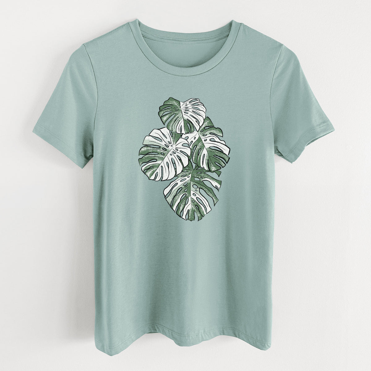 Dusty blue women's relaxed fit cotton t-shirt laid flat, printed with a full-color illustration of a variegated Monstera leaf in green and white.