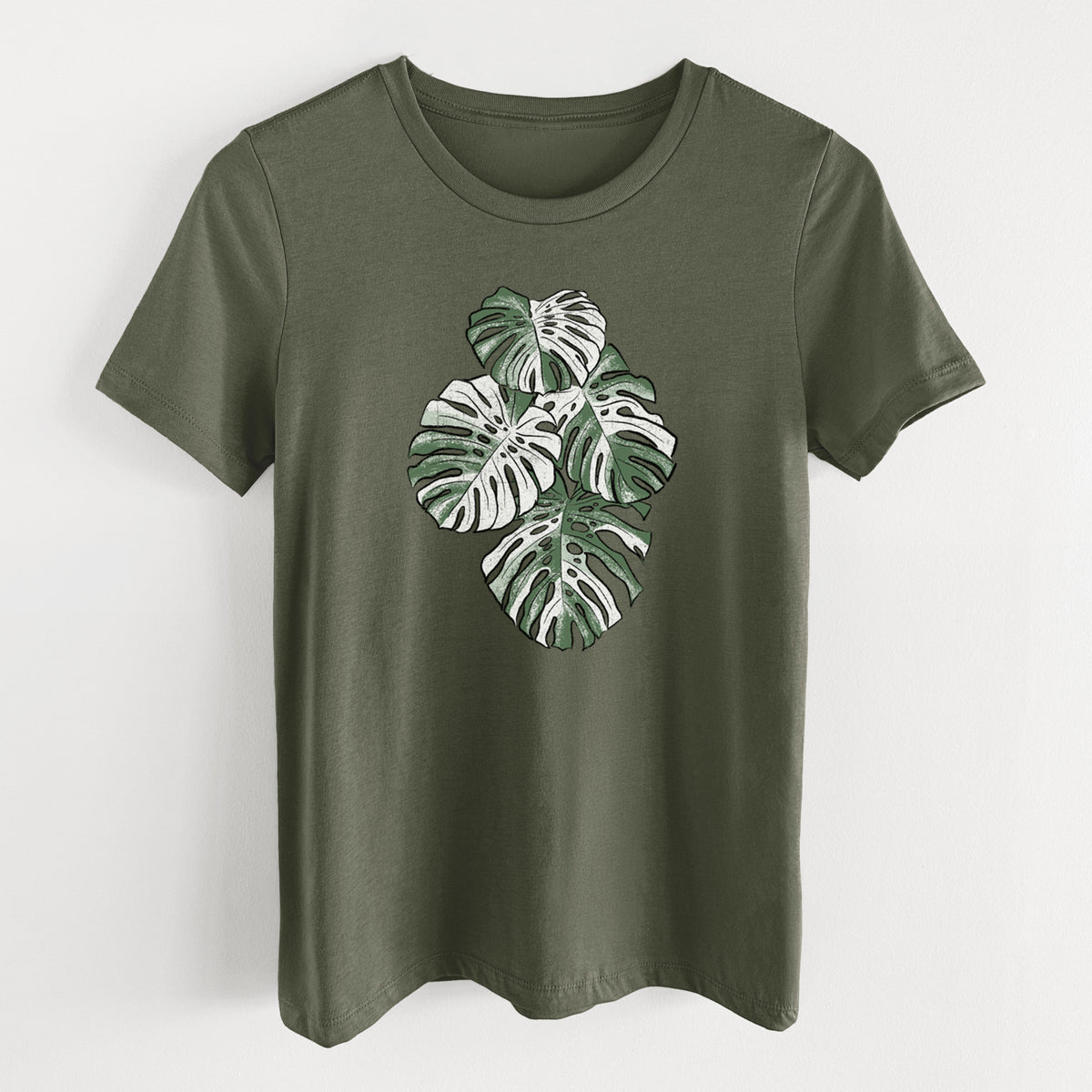 Military green women's relaxed fit cotton t-shirt laid flat, printed with a full-color illustration of a variegated Monstera leaf in green and white.