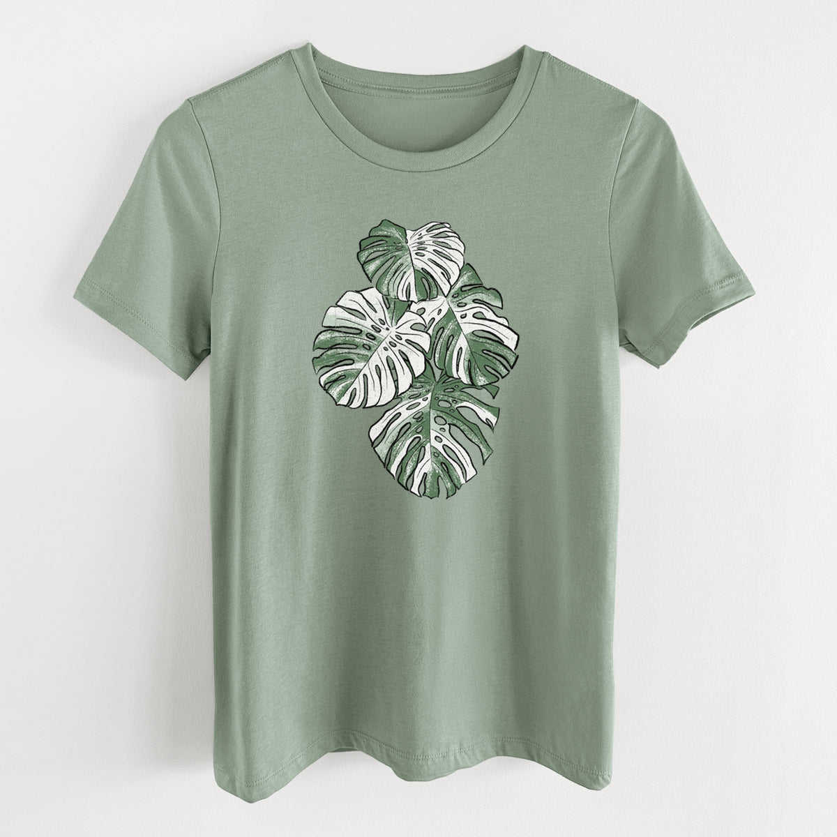 Sage green women's relaxed fit cotton t-shirt laid flat, printed with a full-color illustration of a variegated Monstera leaf in green and white.