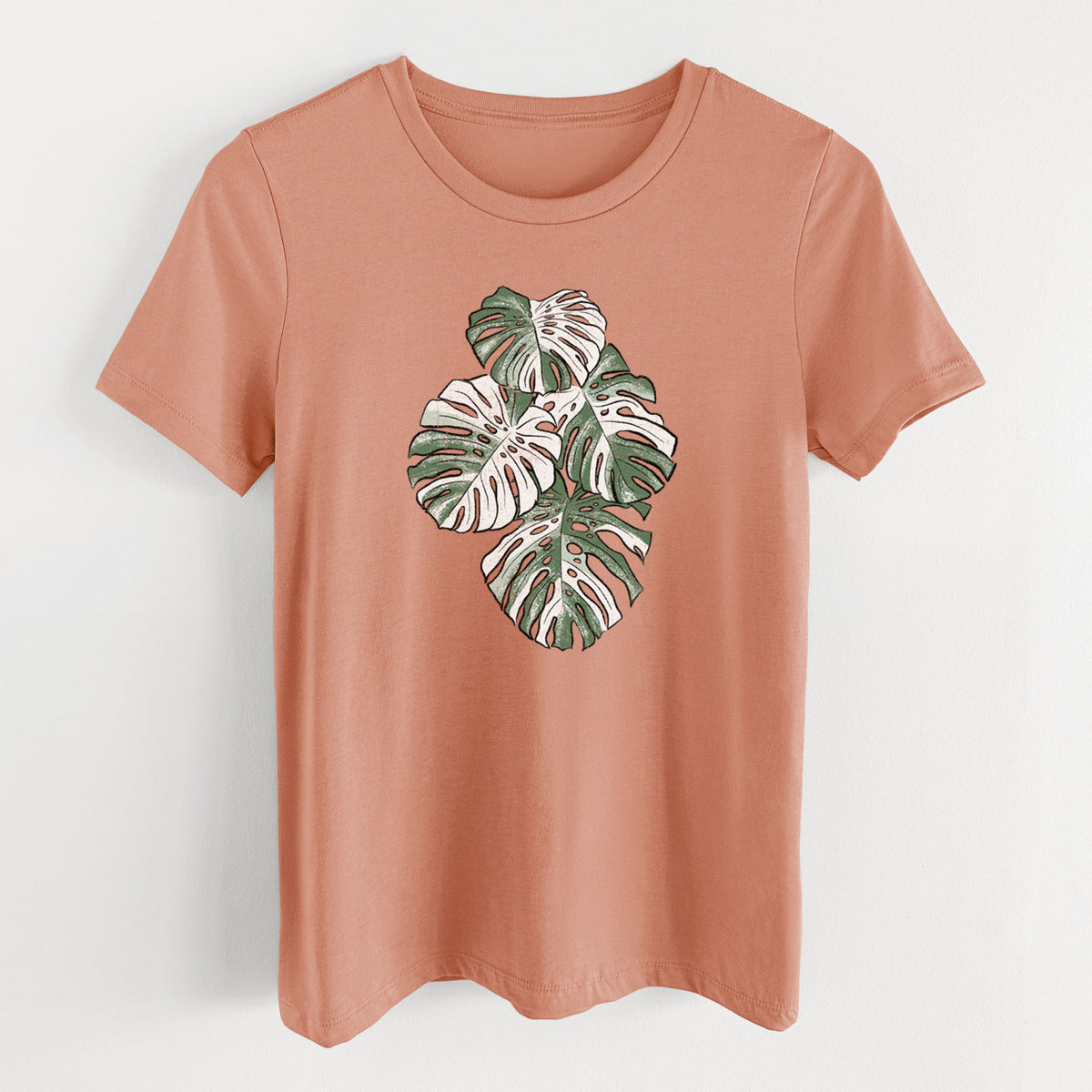 Terracotta orange women's relaxed fit cotton t-shirt laid flat, printed with a full-color illustration of a variegated Monstera leaf in green and white.