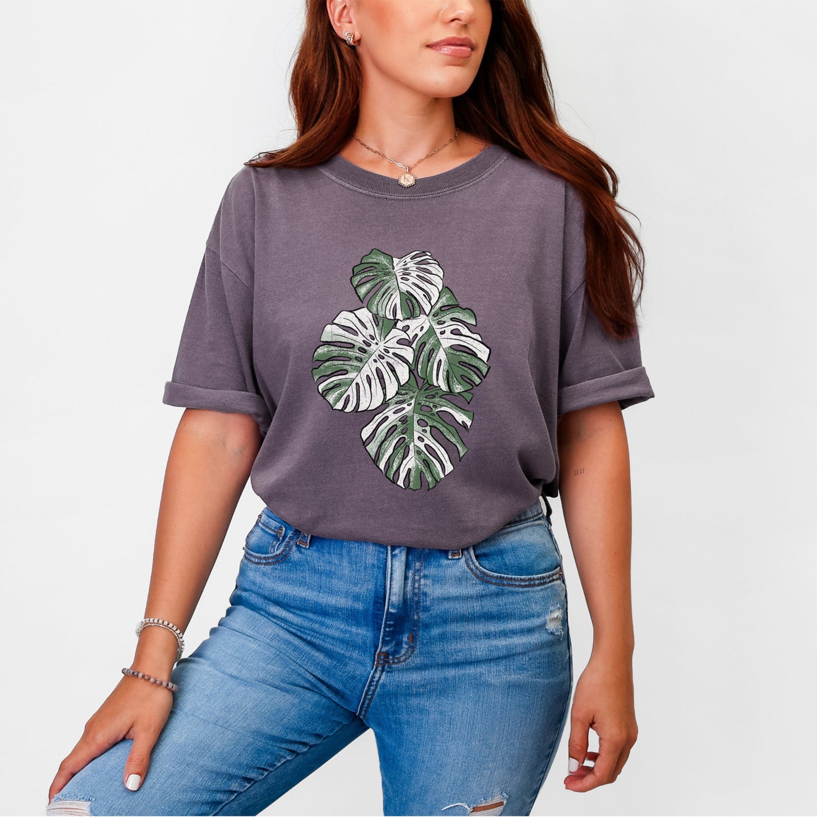 Blue jean Comfort Colors t-shirt laid flat, printed with a full-color illustration of a variegated Monstera leaf in green and white.