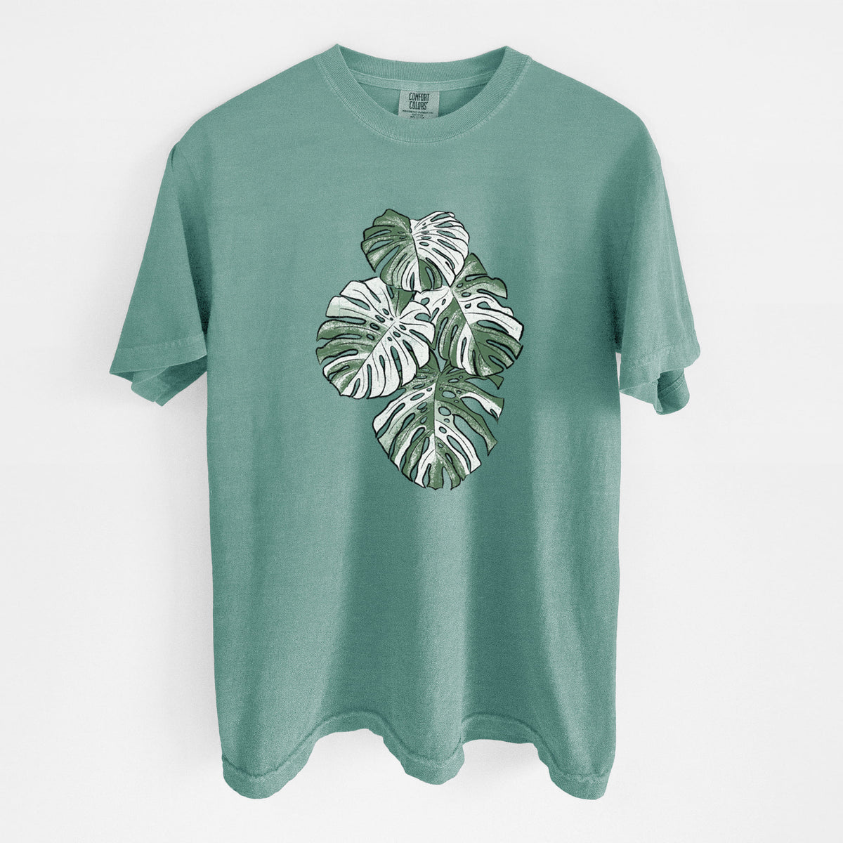 Reef green Comfort Colors t-shirt laid flat, printed with a full-color illustration of a variegated Monstera leaf in green and white.