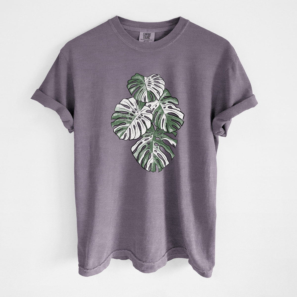 Wine red Comfort Colors t-shirt laid flat, printed with a full-color illustration of a variegated Monstera leaf in green and white.