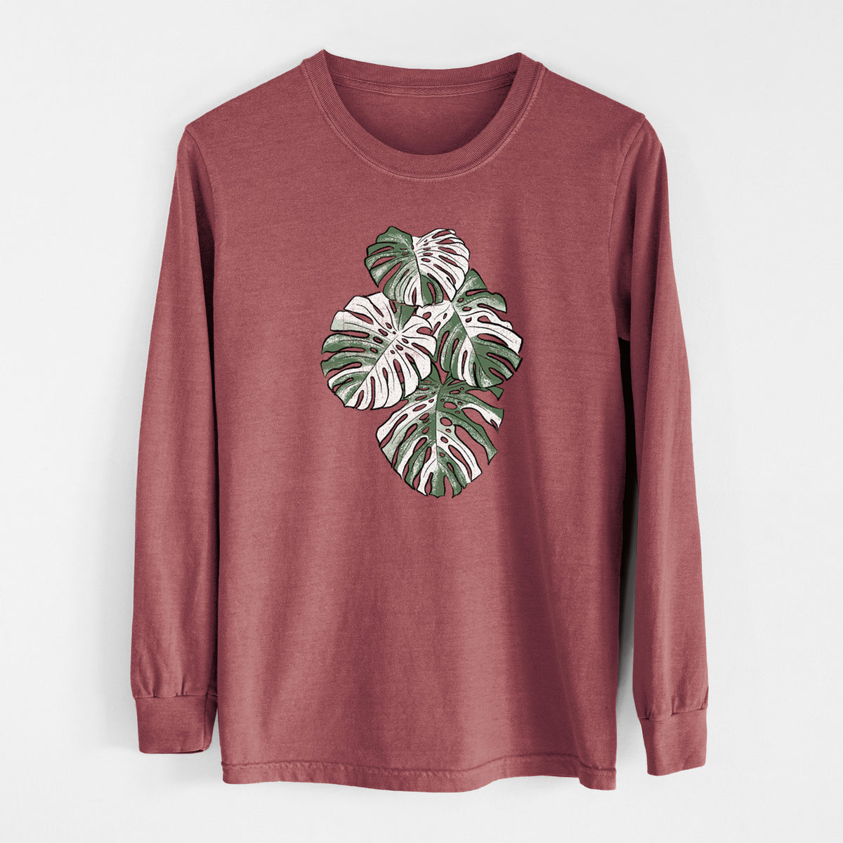 Brick red Comfort Colors long sleeve shirt laid flat, printed with a full-color illustration of a variegated Monstera leaf in green and white.