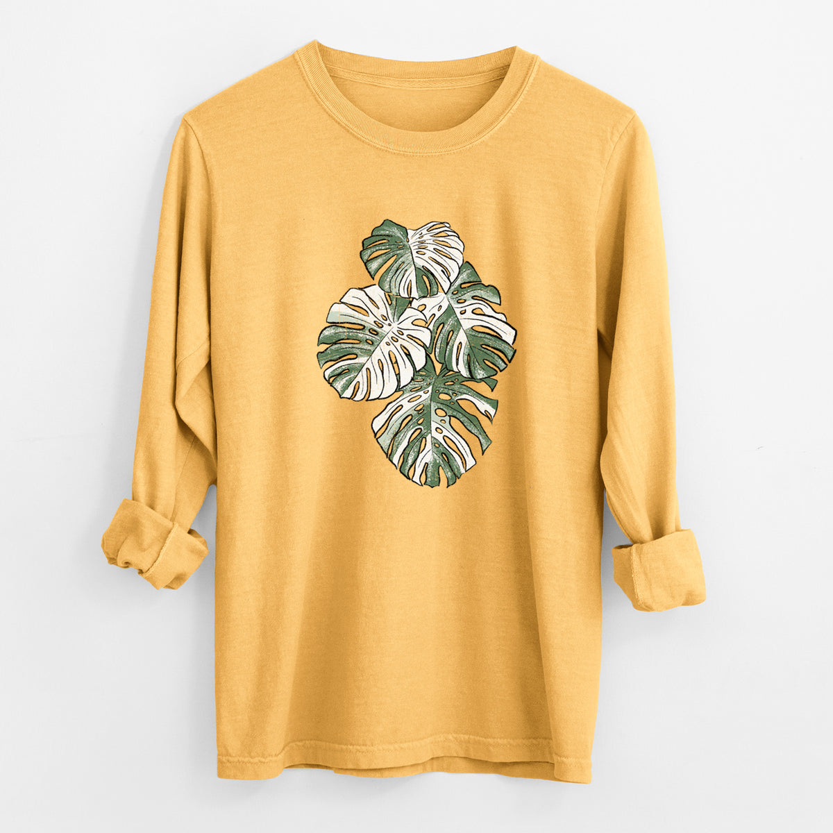 Golden wheat yellow Comfort Colors long sleeve shirt laid flat with the cuffs rolled, printed with a full-color illustration of a variegated Monstera leaf in green and white.