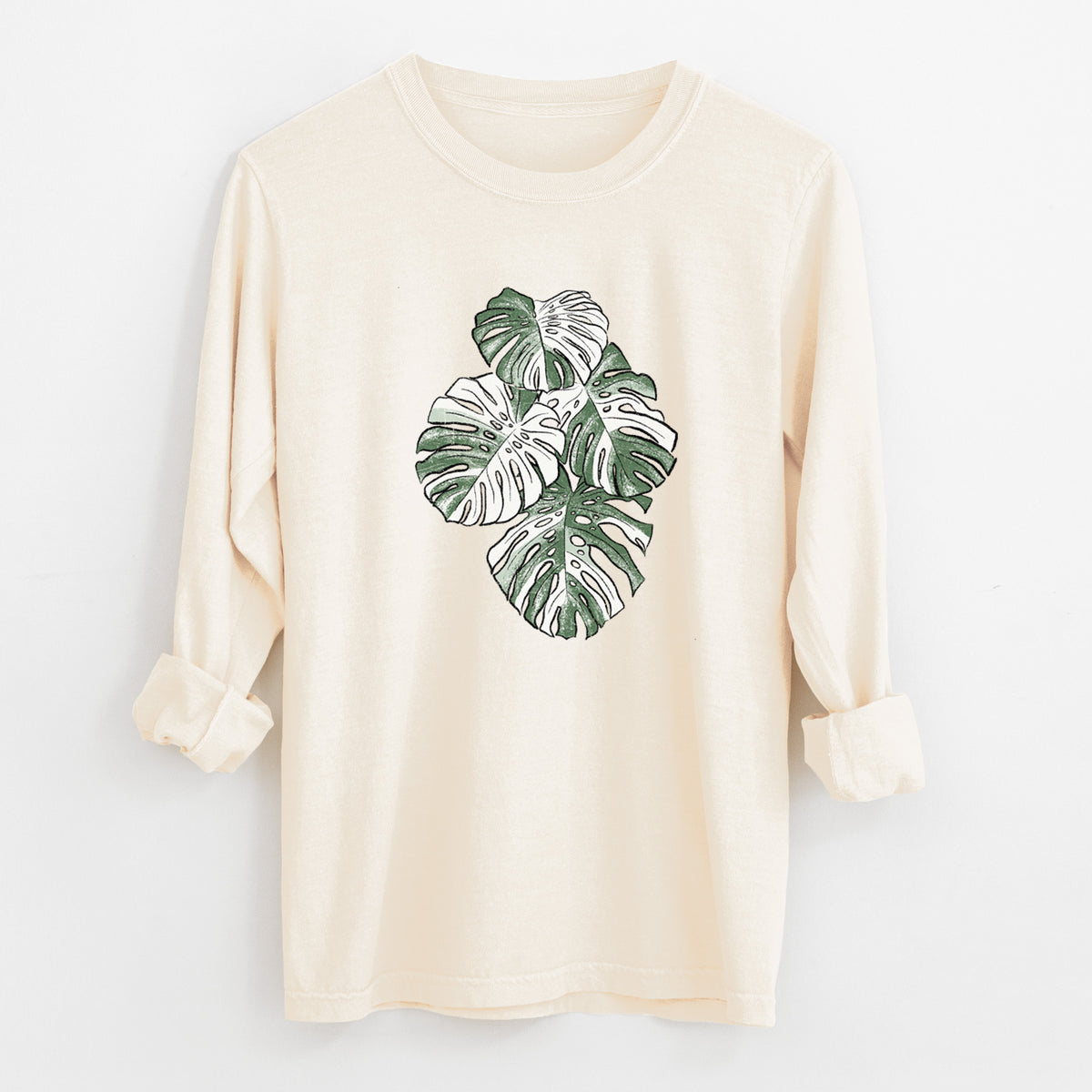 Ivory Comfort Colors long sleeve shirt laid flat with the cuffs rolled, printed with a full-color illustration of a variegated Monstera leaf in green and white.