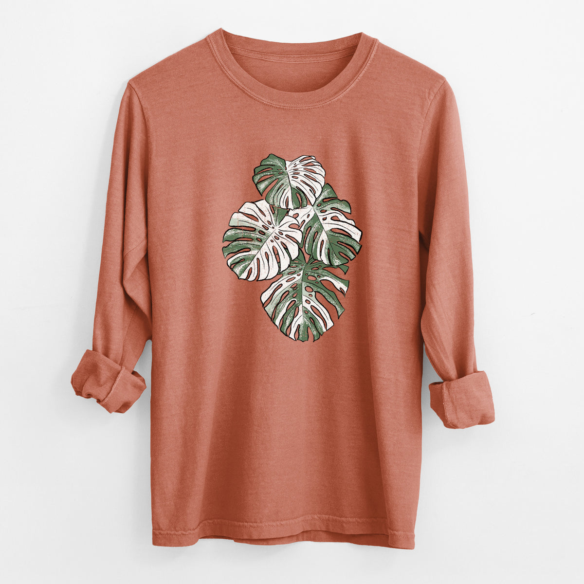 Yam burnt orange Comfort Colors long sleeve shirt laid flat with the cuffs rolled, printed with a full-color illustration of a variegated Monstera leaf in green and white.
