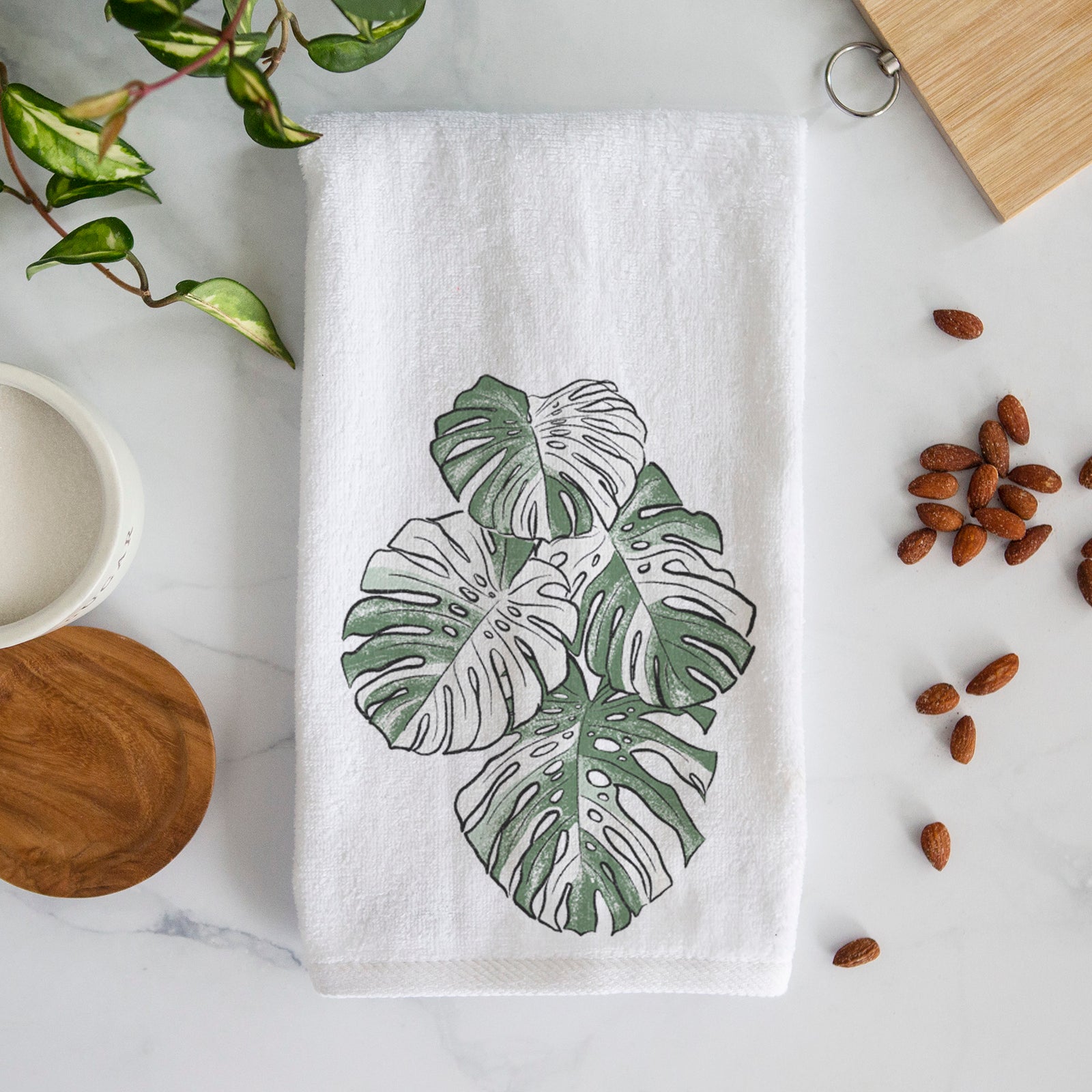 White hand towel printed with a full-color illustration of a variegated Monstera leaf in green and white.