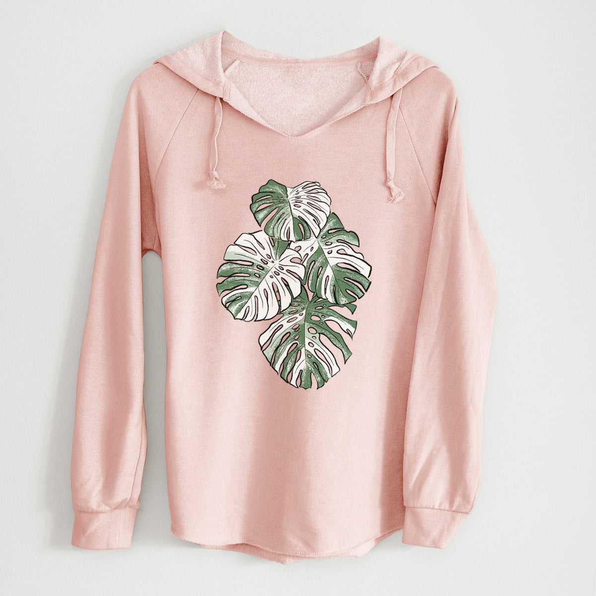 Blush pink women's Cali Wave hooded sweatshirt laid flat, printed with a full-color illustration of a variegated Monstera leaf in green and white.