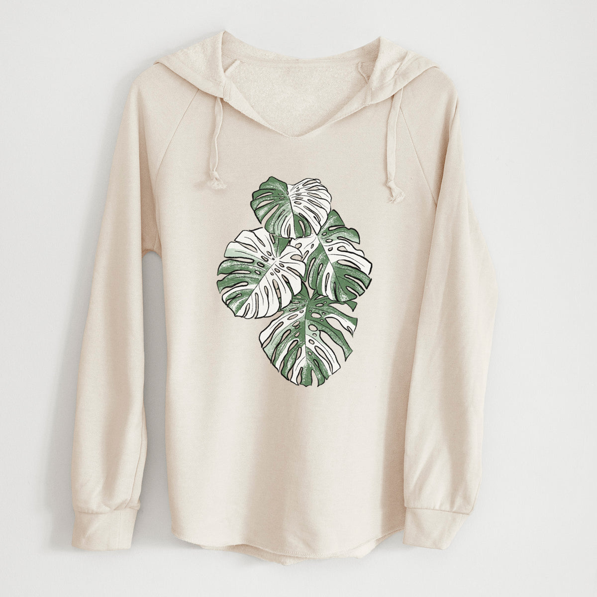 Bone cream women's Cali Wave hooded sweatshirt laid flat, printed with a full-color illustration of a variegated Monstera leaf in green and white.