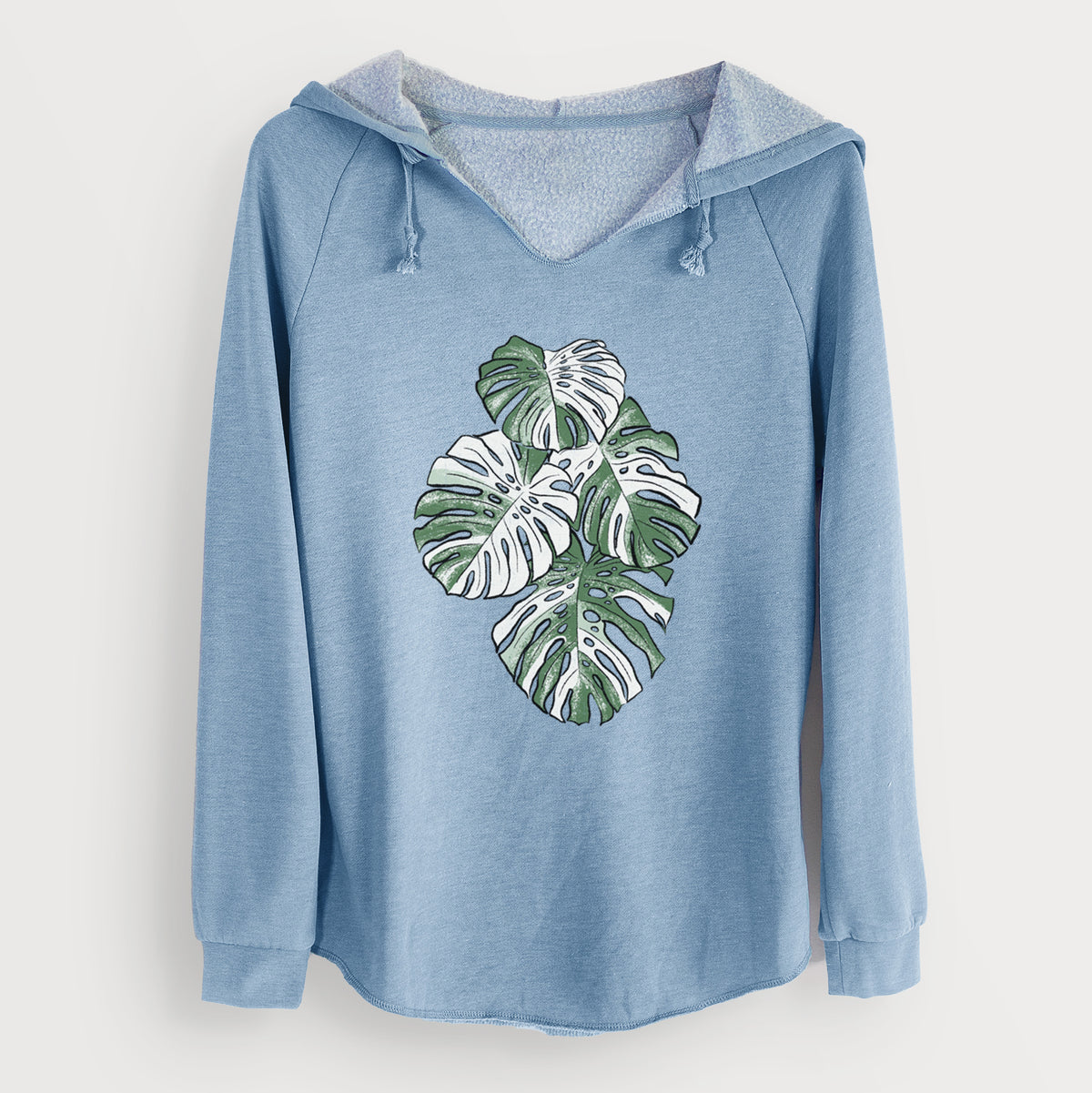 Misty blue women's Cali Wave hooded sweatshirt laid flat, printed with a full-color illustration of a variegated Monstera leaf in green and white.