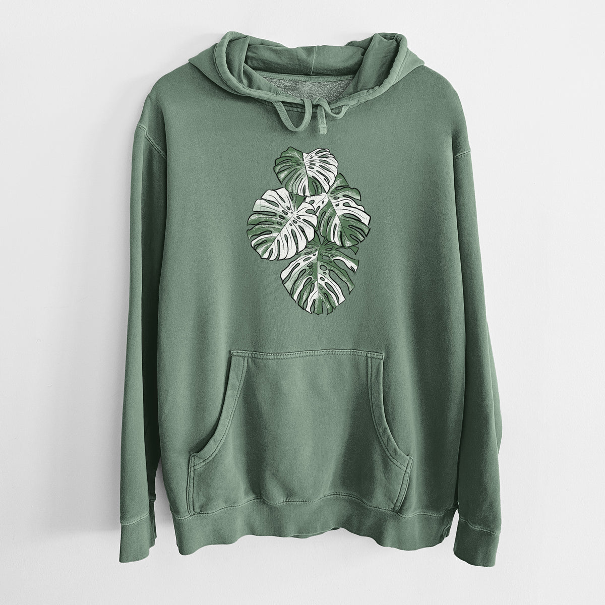 Alpine green pigment dyed hoodie laid flat, printed with a full-color illustration of a variegated Monstera leaf in green and white.