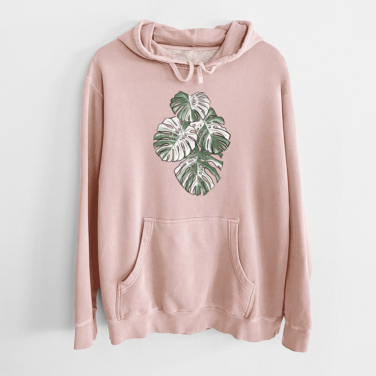Dusty pink pigment dyed hoodie laid flat, printed with a full-color illustration of a variegated Monstera leaf in green and white.