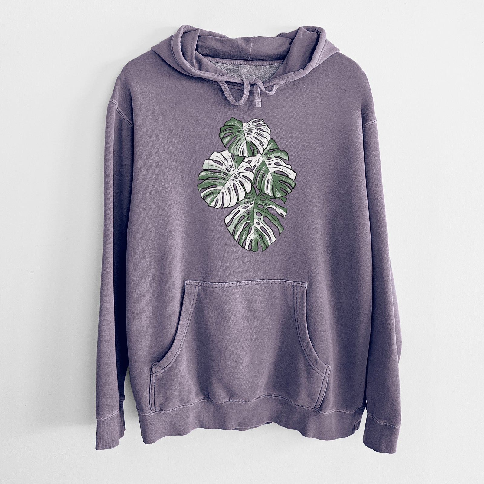 Plum purple pigment dyed hoodie laid flat, printed with a full-color illustration of a variegated Monstera leaf in green and white.