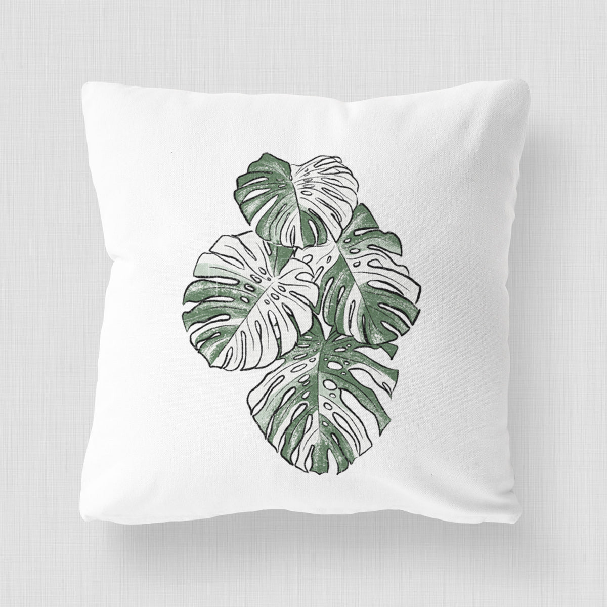 White pillow cover printed with a full-color illustration of a variegated Monstera leaf in green and white.
