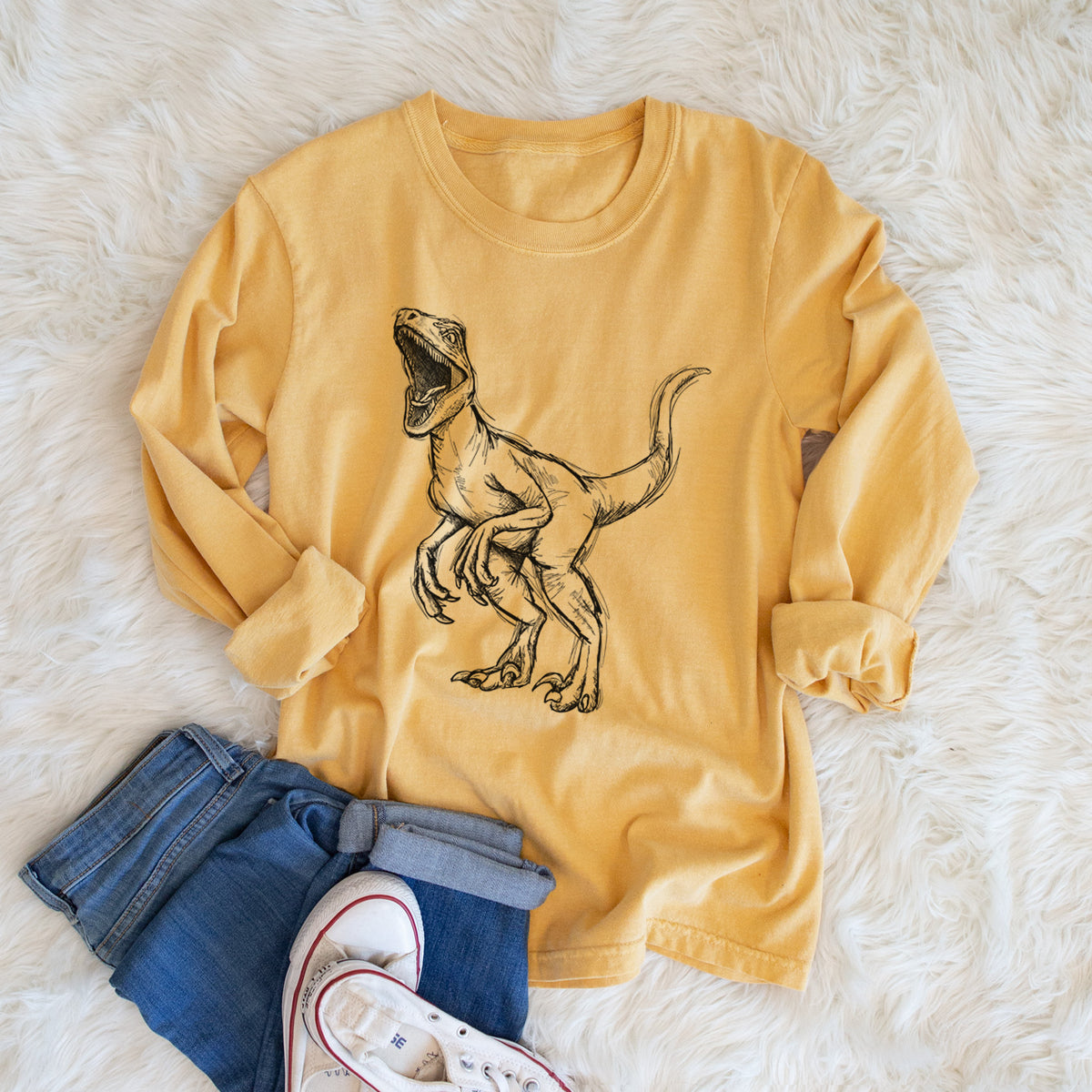 Golden wheat yellow Comfort Colors long sleeve shirt printed with a black ink illustration of a Velociraptor roaring, shown in a lifestyle photo.