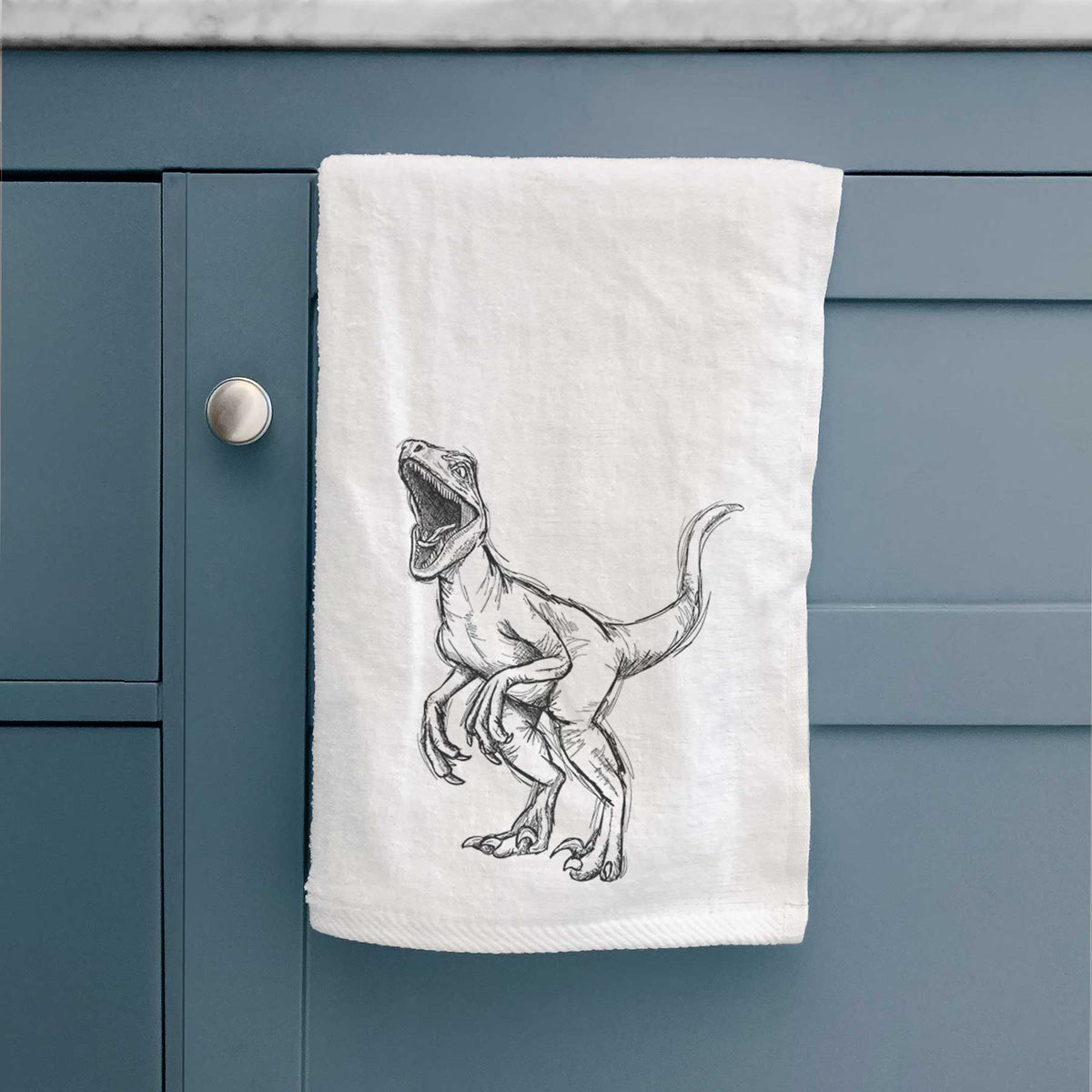 White hand towel printed with a black ink illustration of a Velociraptor roaring.