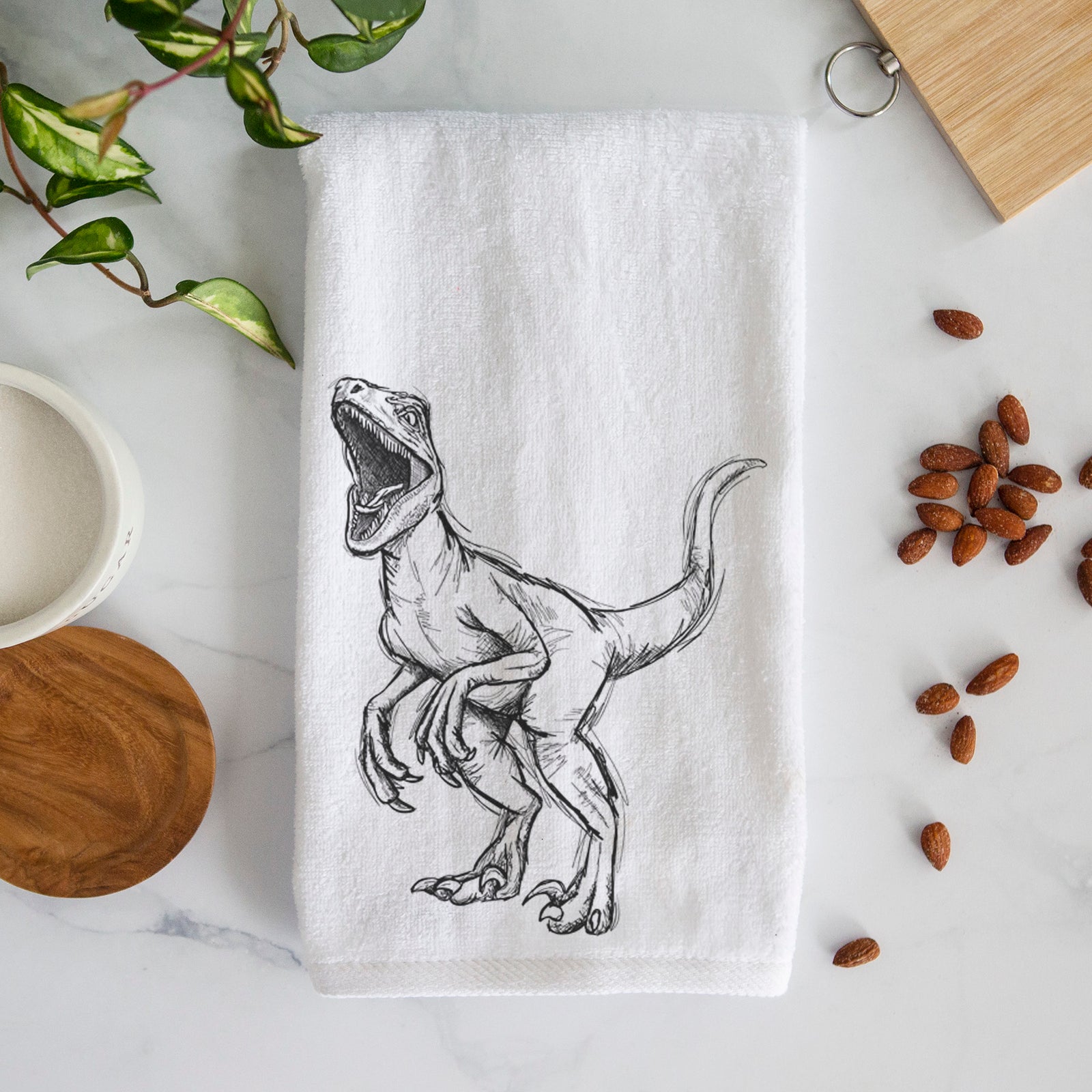 White hand towel printed with a black ink illustration of a Velociraptor roaring.