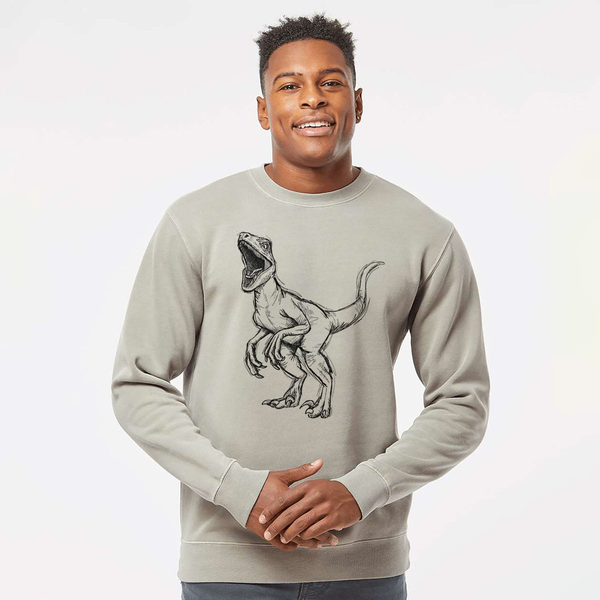 Model wearing a cement grey pigment dyed crewneck sweatshirt printed with a black ink illustration of a Velociraptor roaring.