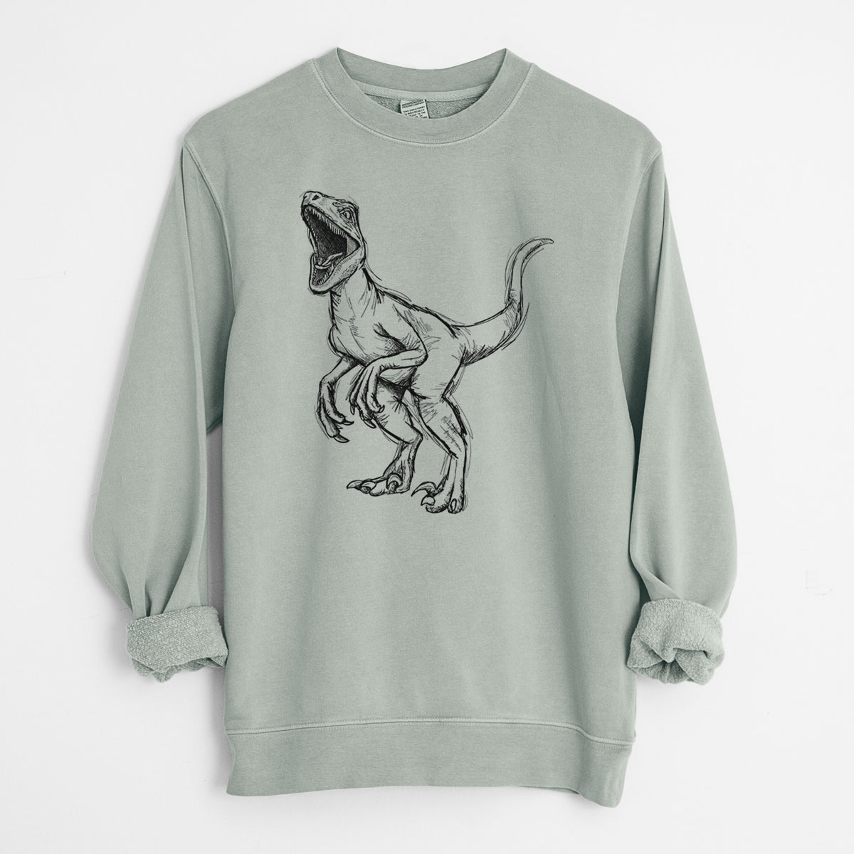 Sage green pigment dyed crewneck sweatshirt laid flat with the sleeves rolled, printed with a black ink illustration of a Velociraptor roaring.