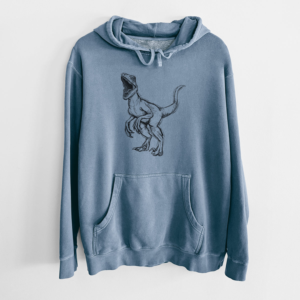Slate blue pigment dyed hoodie laid flat, printed with a black ink illustration of a Velociraptor roaring.