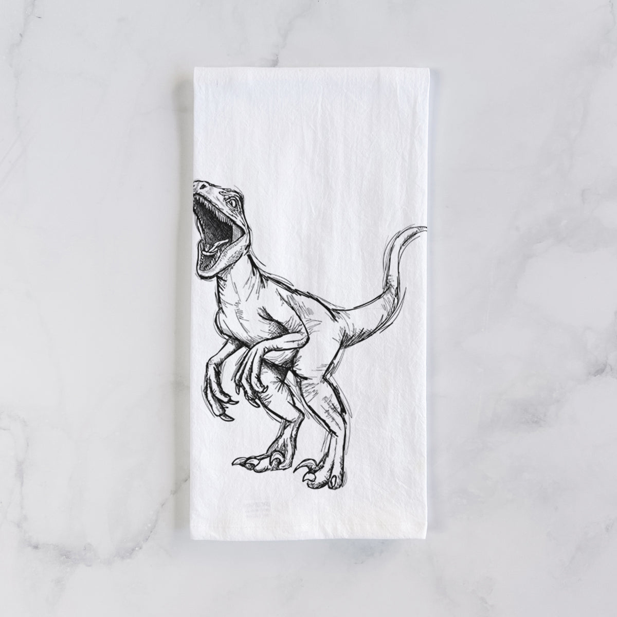 White cotton tea towel laid flat on marble, printed with a black ink illustration of a Velociraptor roaring.