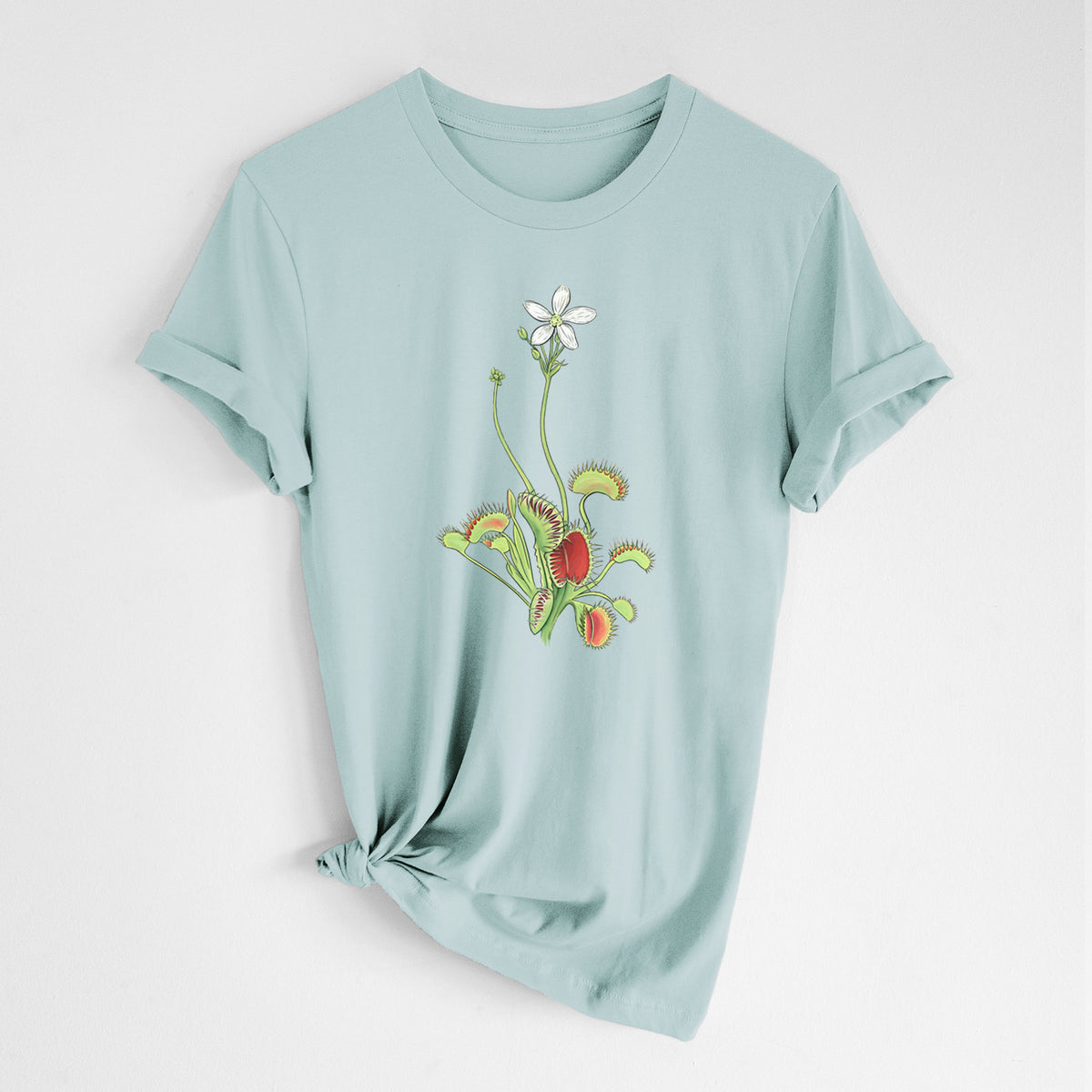 Dusty blue lightweight cotton t-shirt laid flat with the sleeves rolled, printed with a full-color illustration of a Venus flytrap plant with red traps and a small white flower.