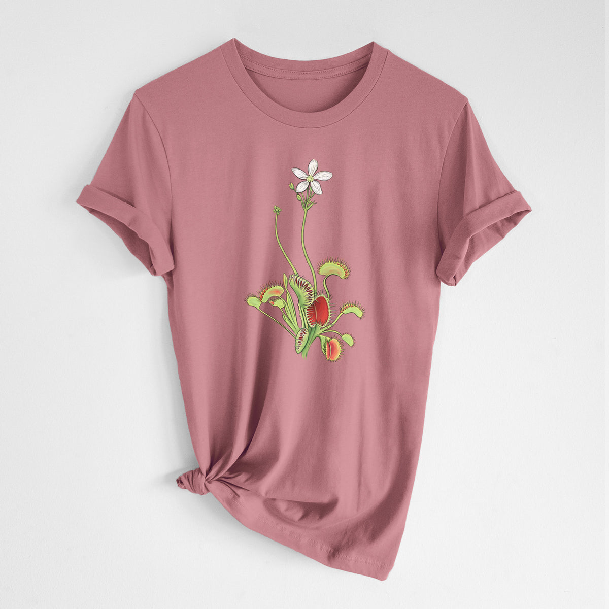 Mauve pink lightweight cotton t-shirt laid flat with the sleeves rolled, printed with a full-color illustration of a Venus flytrap plant with red traps and a small white flower.