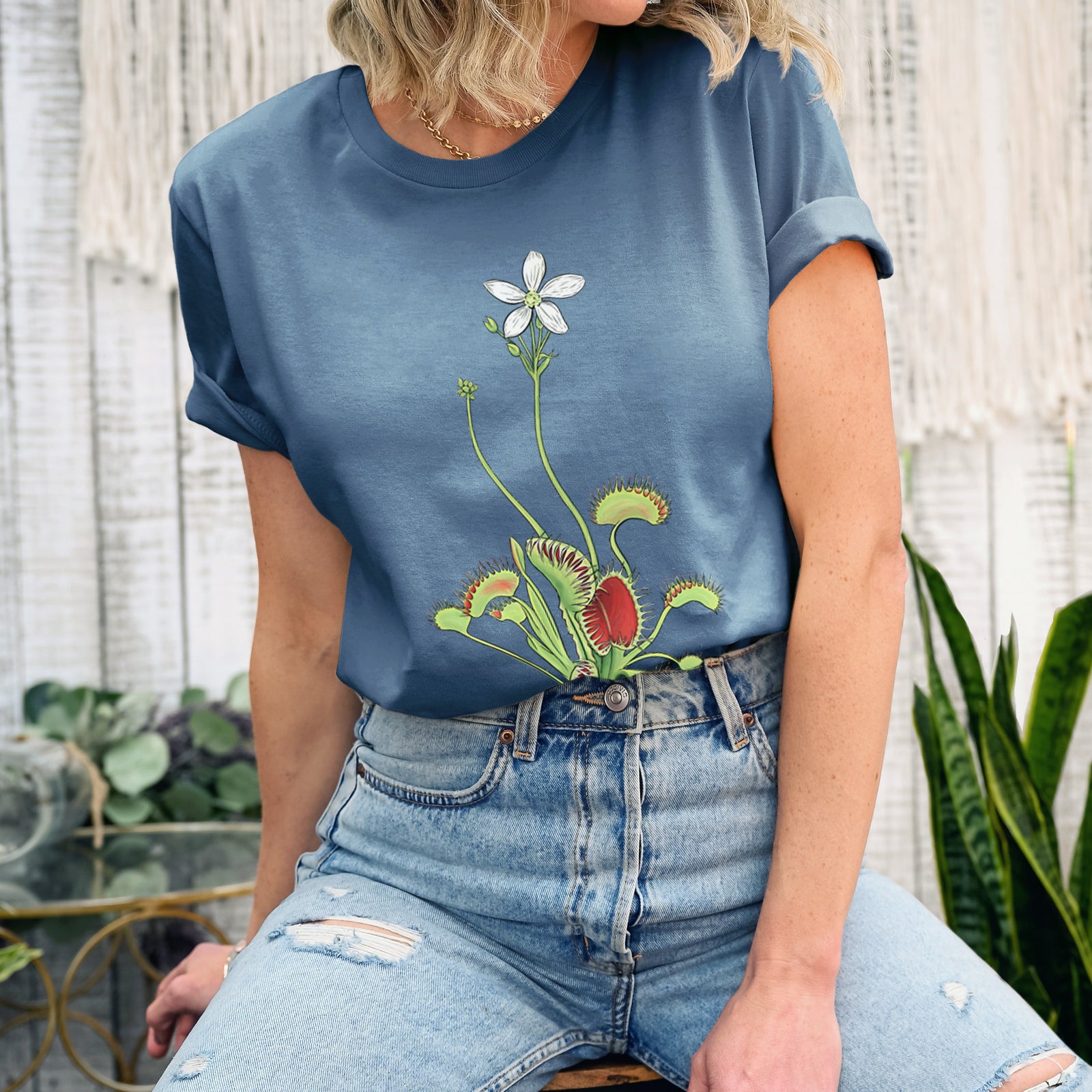 Autumn lightweight cotton t-shirt laid flat, printed with a full-color illustration of a Venus flytrap plant with red traps and a small white flower.
