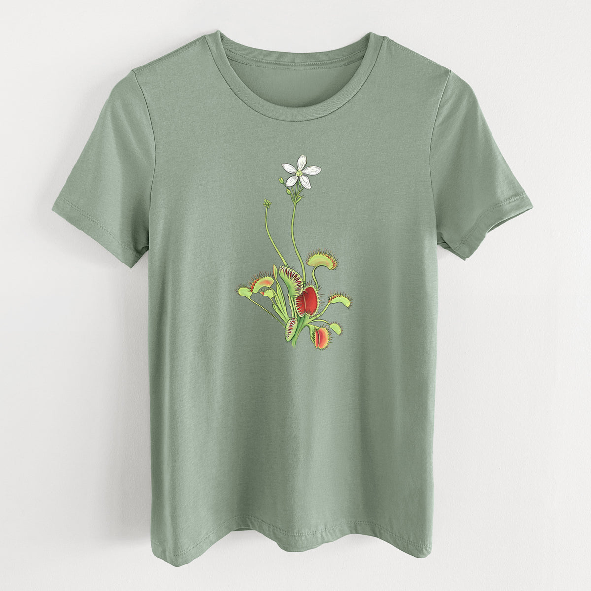 Sage green women's relaxed fit cotton t-shirt laid flat, printed with a full-color illustration of a Venus flytrap plant with red traps and a small white flower.