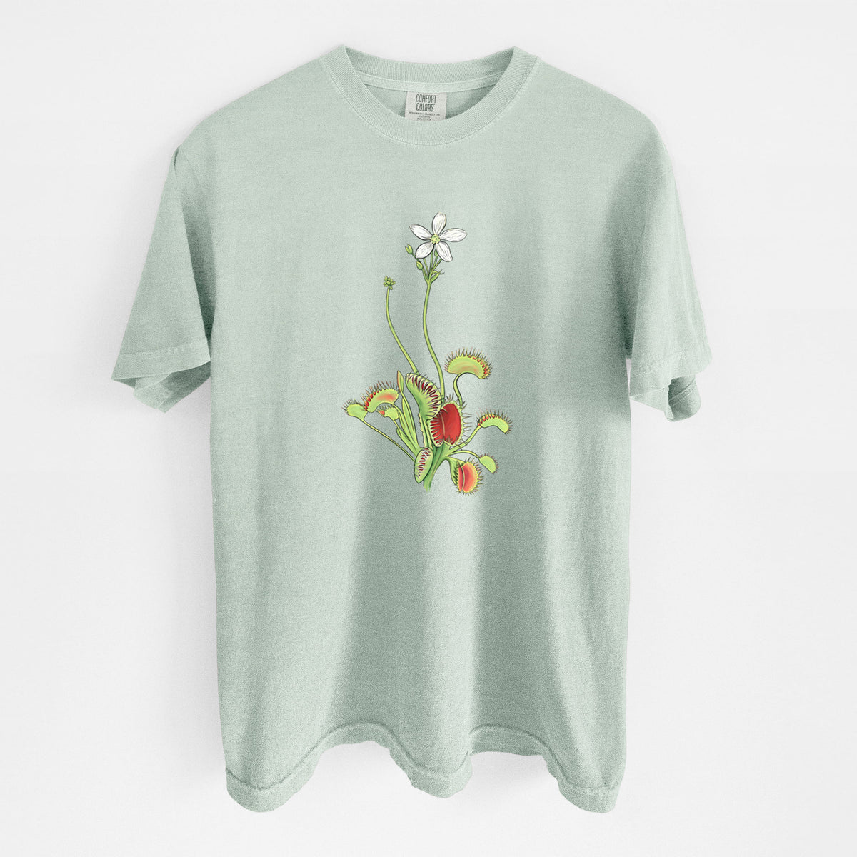 Bay green Comfort Colors t-shirt laid flat, printed with a full-color illustration of a Venus flytrap plant with red traps and a small white flower.