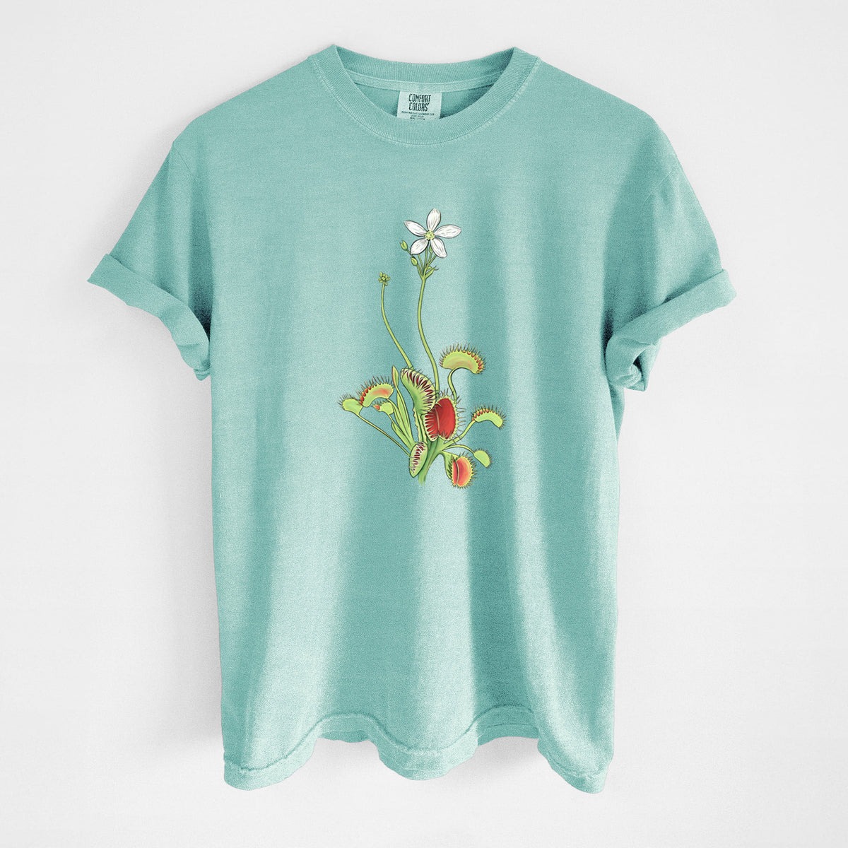 Chalky mint Comfort Colors t-shirt laid flat, printed with a full-color illustration of a Venus flytrap plant with red traps and a small white flower.