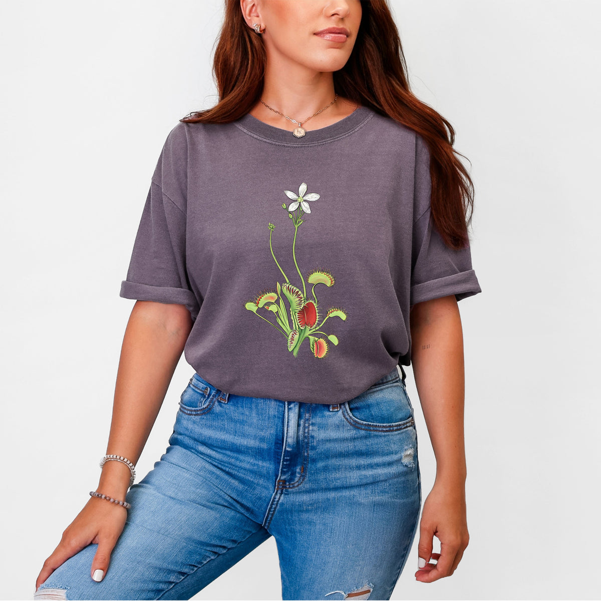 Woman wearing a Comfort Colors t-shirt printed with a full-color illustration of a Venus flytrap plant with red traps and a small white flower.