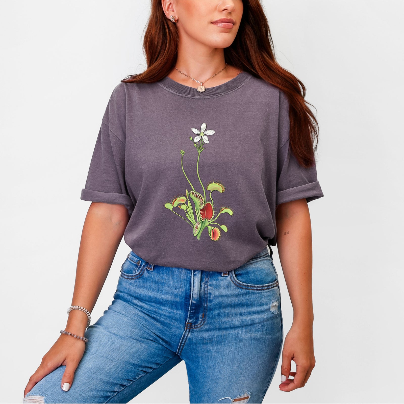 Blue jean Comfort Colors t-shirt laid flat, printed with a full-color illustration of a Venus flytrap plant with red traps and a small white flower.