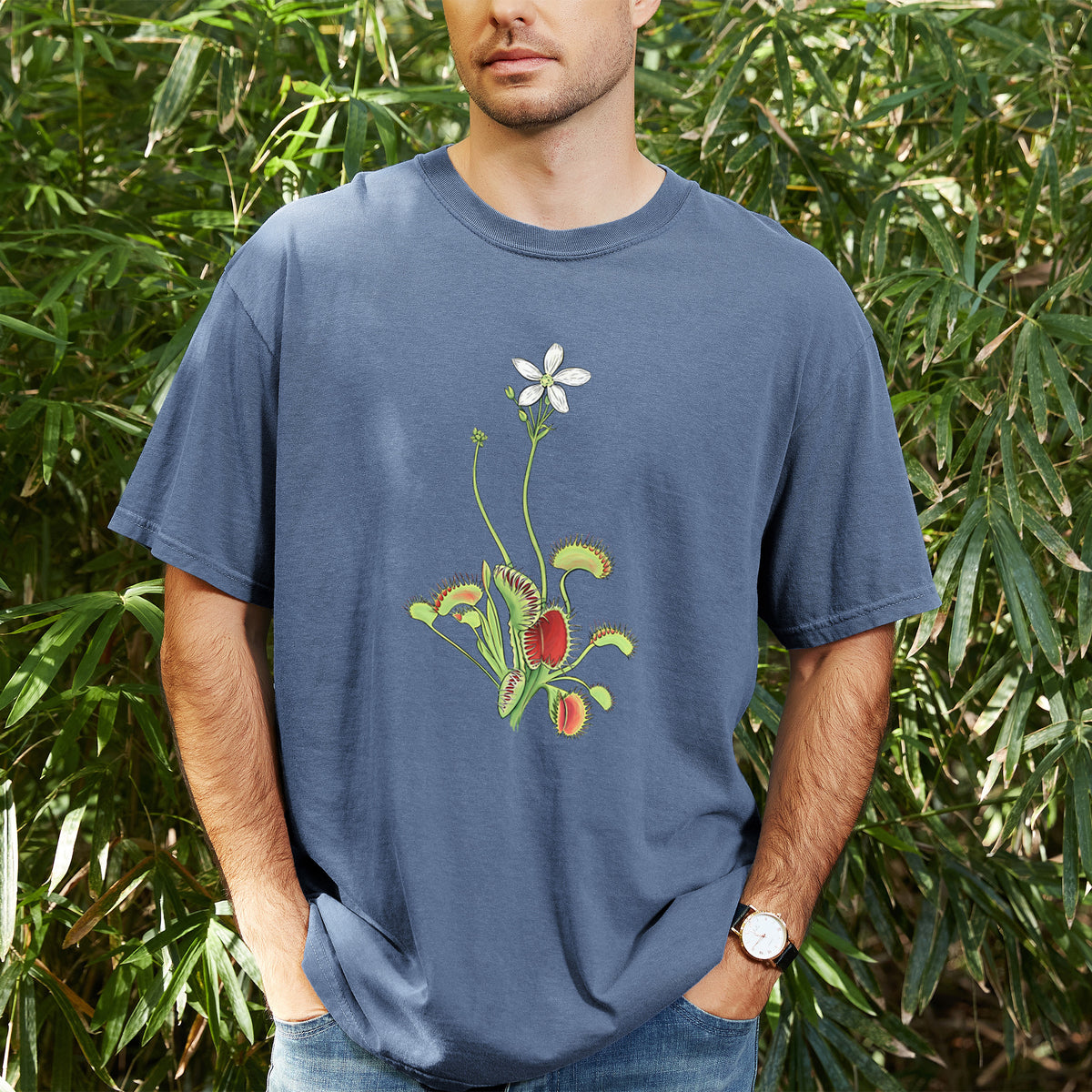 Man wearing a Comfort Colors t-shirt printed with a full-color illustration of a Venus flytrap plant with red traps and a small white flower, outdoors.