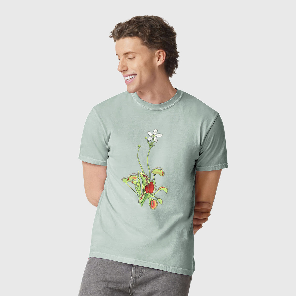 Man wearing a Comfort Colors t-shirt printed with a full-color illustration of a Venus flytrap plant with red traps and a small white flower.