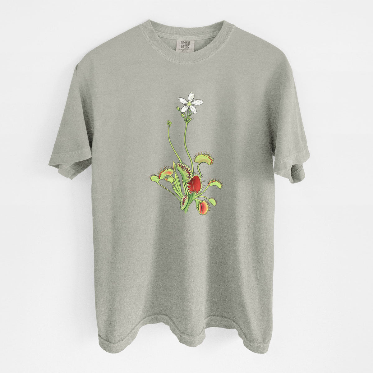 Sandstone beige Comfort Colors t-shirt laid flat, printed with a full-color illustration of a Venus flytrap plant with red traps and a small white flower.