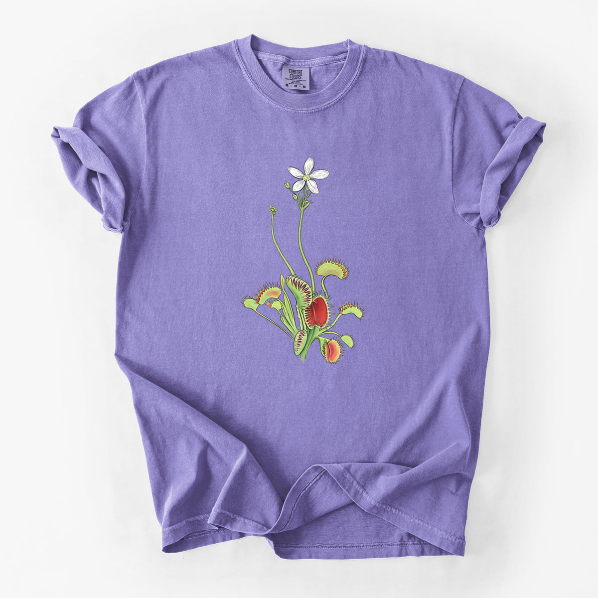 Violet purple Comfort Colors t-shirt laid flat, printed with a full-color illustration of a Venus flytrap plant with red traps and a small white flower.