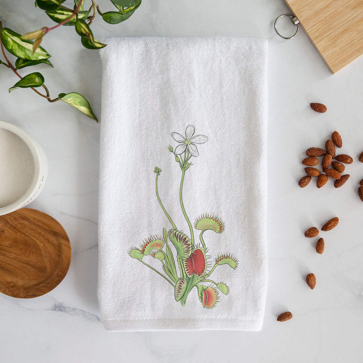 White hand towel printed with a full-color illustration of a Venus flytrap plant with red traps and a small white flower.